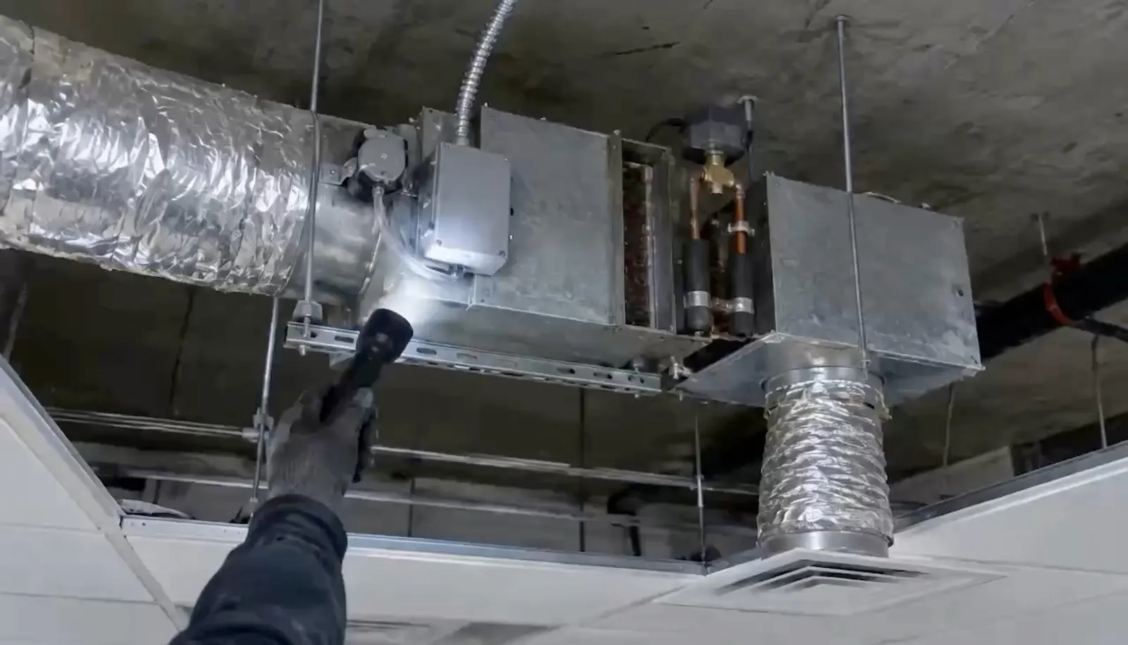 Video: a VAV box in an open ceiling under a flashlight, a technician at a rooftop unit, a pitot tube in a duct.